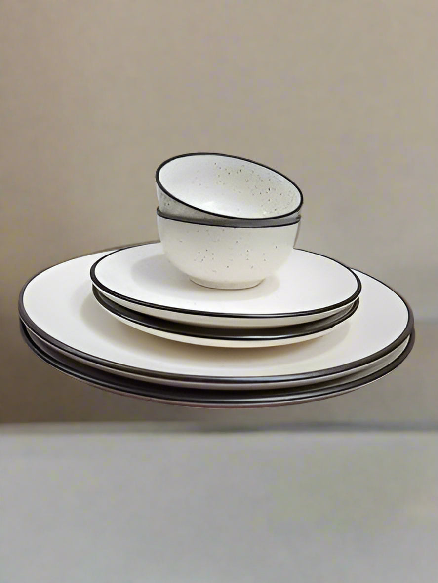6-piece white ceramic dinnerware set with black border, including plates and bowls, displayed on a dining table with a modern minimalist background